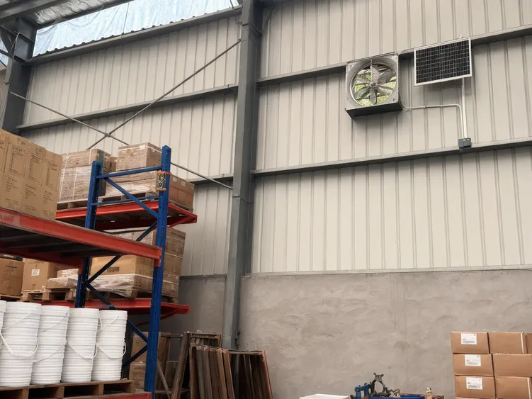 Wall-mounted solar exhaust fan extracting heat from warehouse interior
