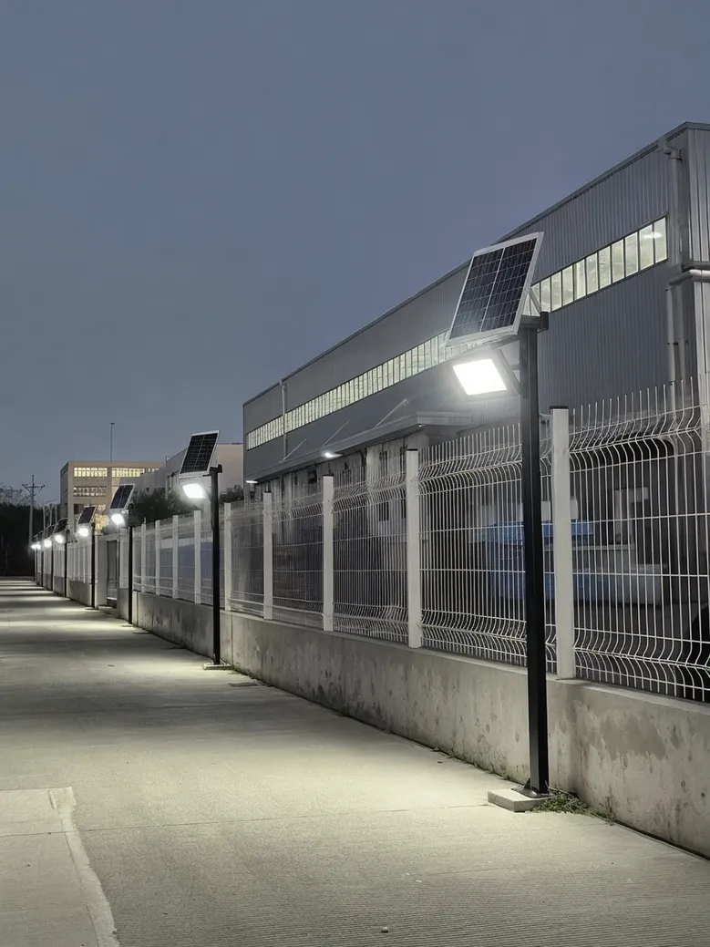 Solar flood lights mounted along a warehouse perimeter fence at dusk