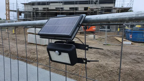 Temporary waterproof solar security light mounted on a construction site perimeter fence