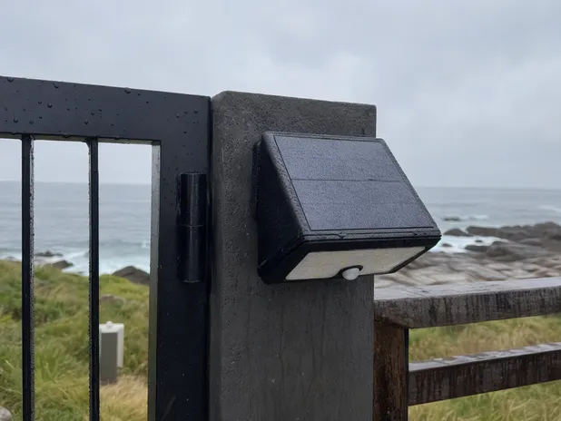 Waterproof solar security light mounted on a coastal property gate post in an exposed wet environment