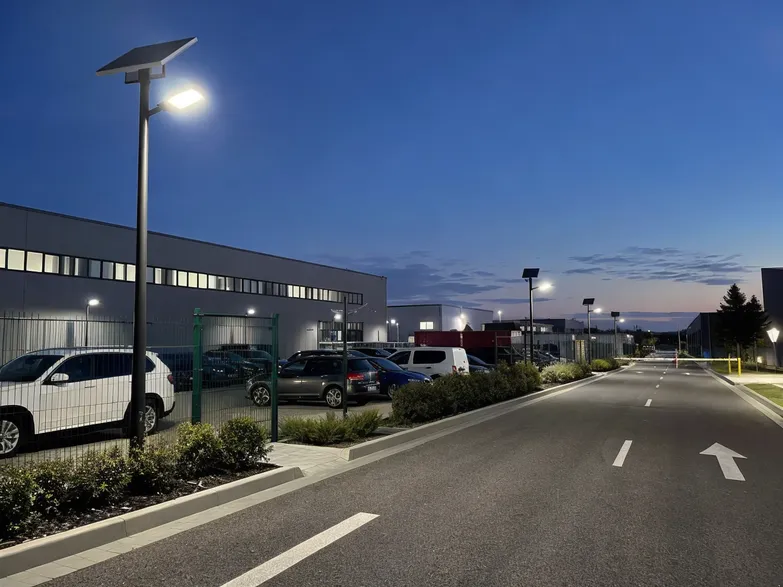 Solar street lights illuminating a commercial parking lot perimeter and access road at dusk
