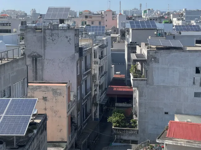 Dense urban street with closely spaced buildings casting shadows on lower walls, solar panels on rooftops above