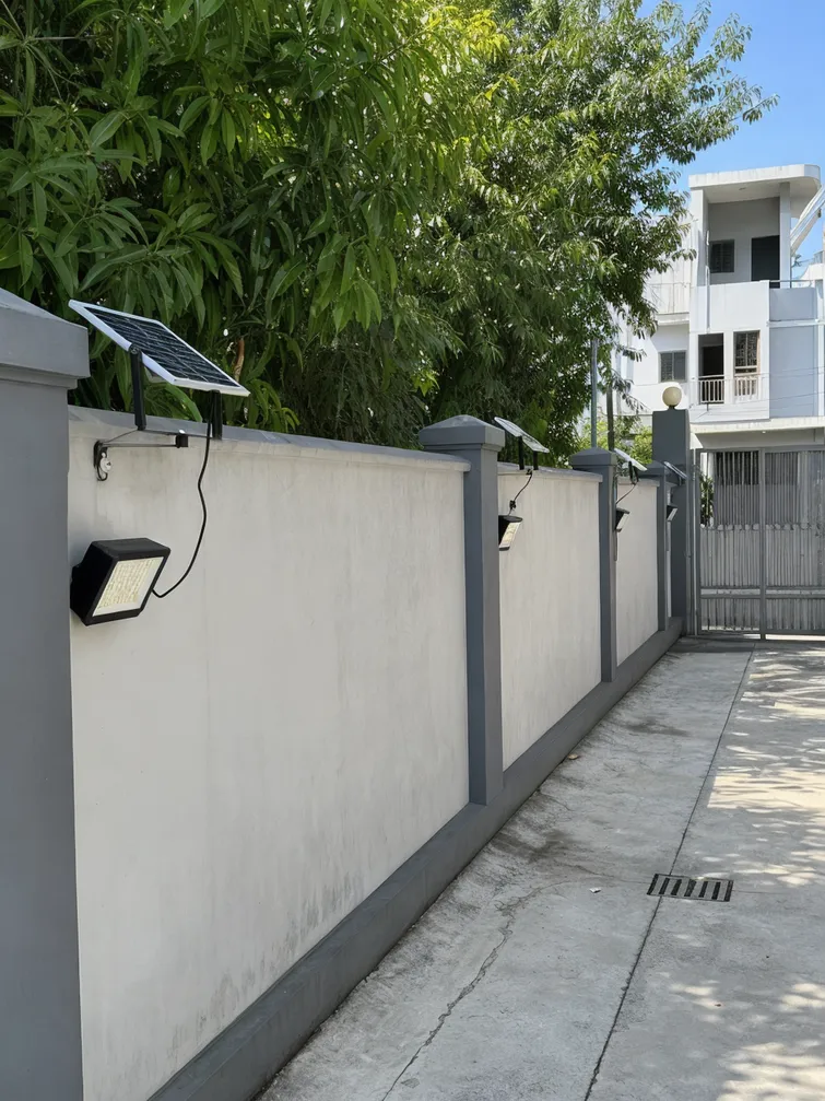 Solar wall lights with separate panels installed along a gated community perimeter wall with mixed sun exposure