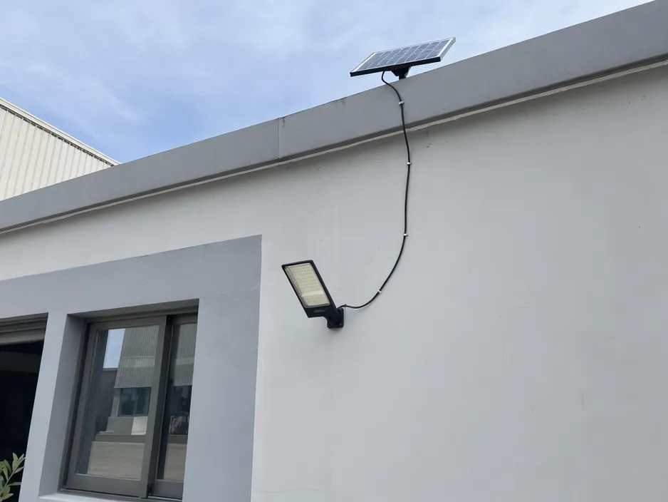 Solar wall light with separate panel mounted on building wall, cable connecting to independently positioned solar panel on roof edge