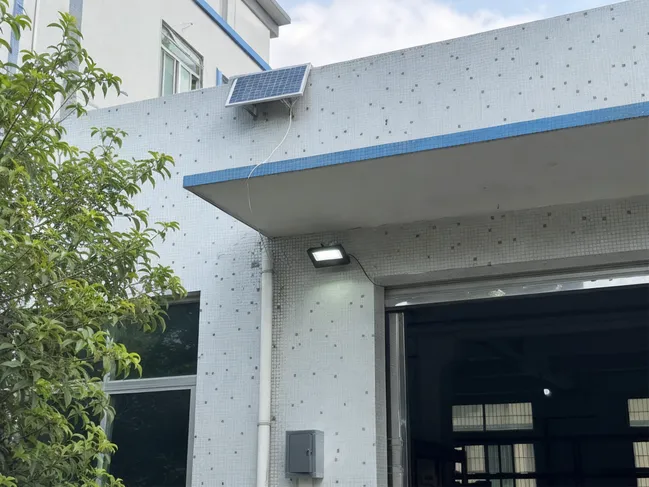 Building entrance with deep overhang shading the wall, solar panel positioned above the canopy in direct sunlight